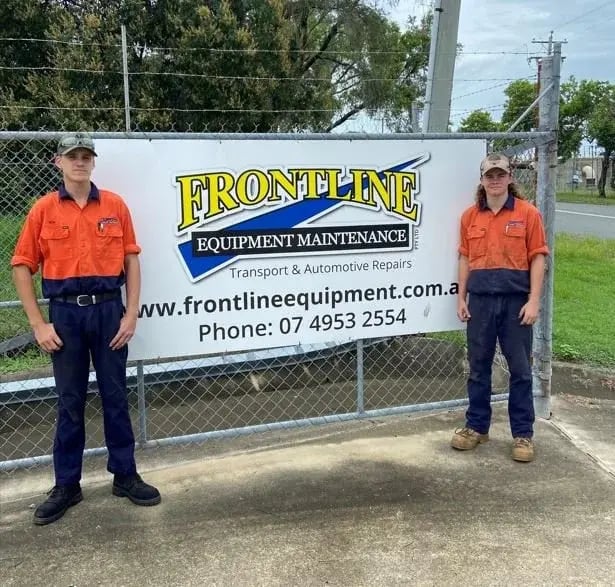 Two Frontline Equipment Maintenance workers in front of their company sign